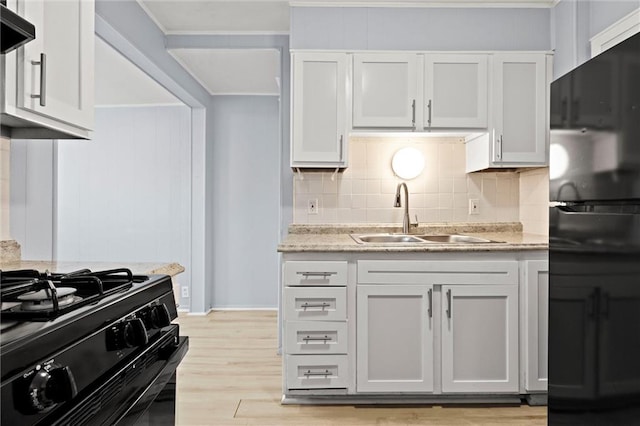 kitchen with sink, tasteful backsplash, light hardwood / wood-style floors, white cabinets, and black appliances