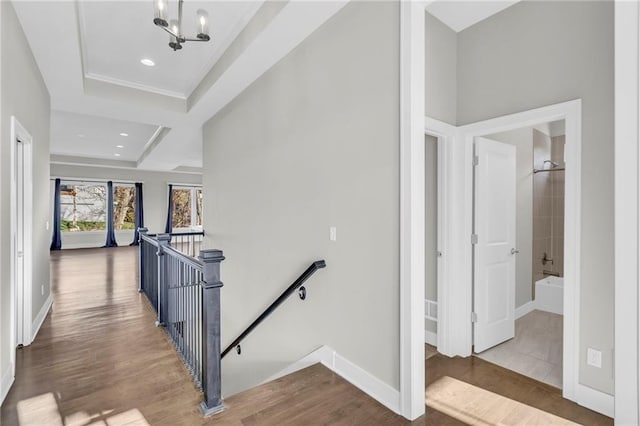 hallway with a tray ceiling, wood-type flooring, and a notable chandelier