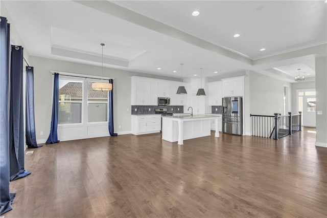 kitchen with appliances with stainless steel finishes, a kitchen island with sink, dark wood-type flooring, white cabinets, and hanging light fixtures