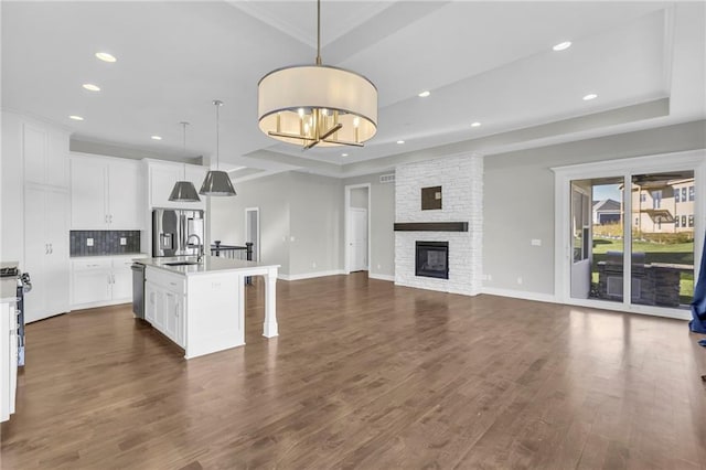 kitchen with dark wood-type flooring, stainless steel refrigerator with ice dispenser, an island with sink, pendant lighting, and white cabinets