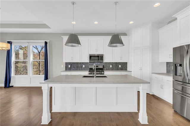 kitchen with sink, hanging light fixtures, dark wood-type flooring, stainless steel appliances, and an island with sink