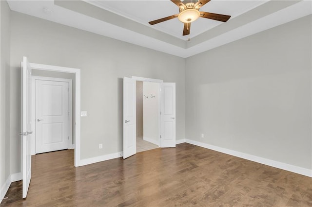 unfurnished bedroom featuring ceiling fan, a raised ceiling, and dark wood-type flooring