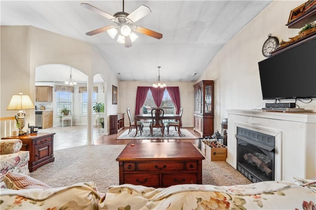 carpeted living area featuring a wealth of natural light, a glass covered fireplace, ceiling fan with notable chandelier, and arched walkways