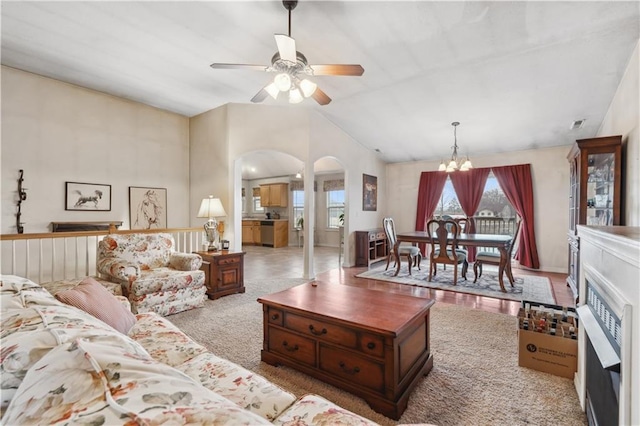 carpeted living area with arched walkways, lofted ceiling, and ceiling fan with notable chandelier