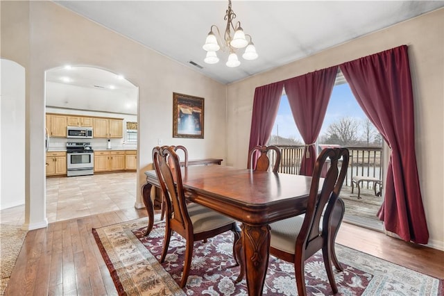 dining area featuring baseboards, visible vents, an inviting chandelier, arched walkways, and light wood-style floors