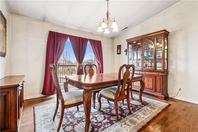 dining space with visible vents, baseboards, lofted ceiling, wood-type flooring, and a notable chandelier