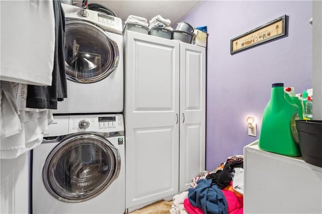 washroom featuring cabinet space, stacked washer and clothes dryer, and a textured wall