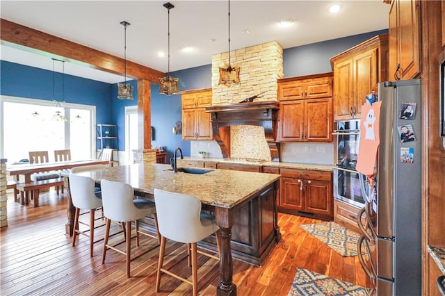 kitchen with dark wood-type flooring, sink, light stone countertops, an island with sink, and stainless steel appliances