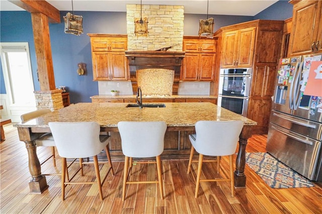 kitchen with pendant lighting, stainless steel appliances, a kitchen island with sink, and light hardwood / wood-style flooring