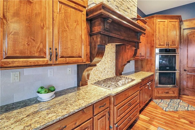 kitchen featuring light stone counters, light wood-type flooring, lofted ceiling, and appliances with stainless steel finishes