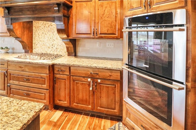 kitchen featuring backsplash, stainless steel appliances, light stone counters, and light hardwood / wood-style floors