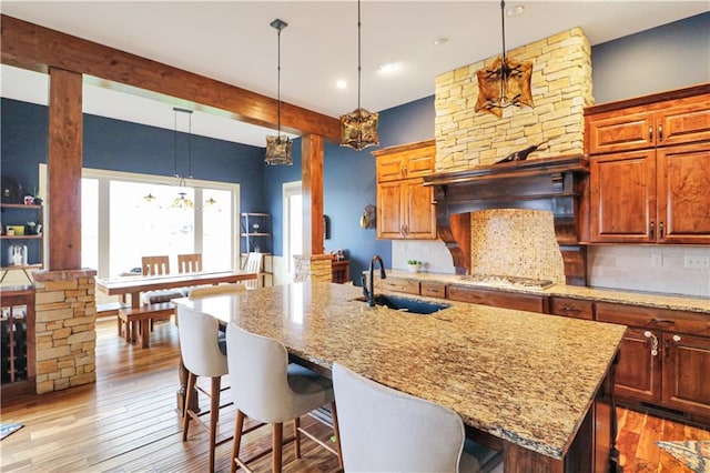 kitchen featuring stainless steel gas stovetop, a center island with sink, a kitchen breakfast bar, sink, and light hardwood / wood-style flooring