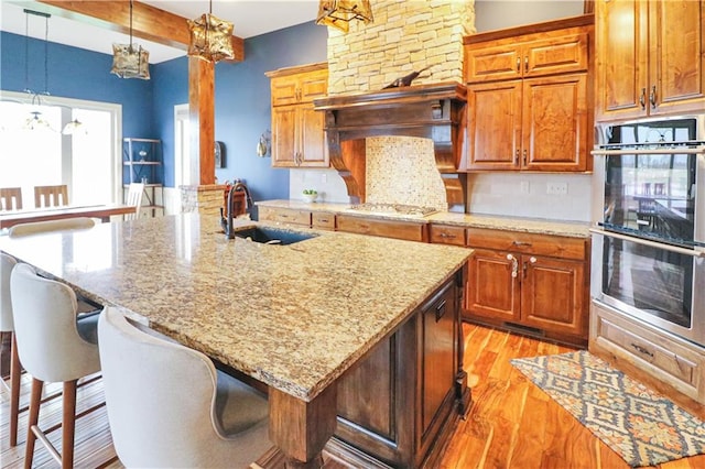 kitchen with stainless steel appliances, sink, an island with sink, and light hardwood / wood-style flooring