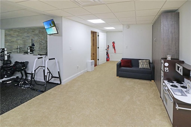 interior space with a paneled ceiling, light colored carpet, and wood walls