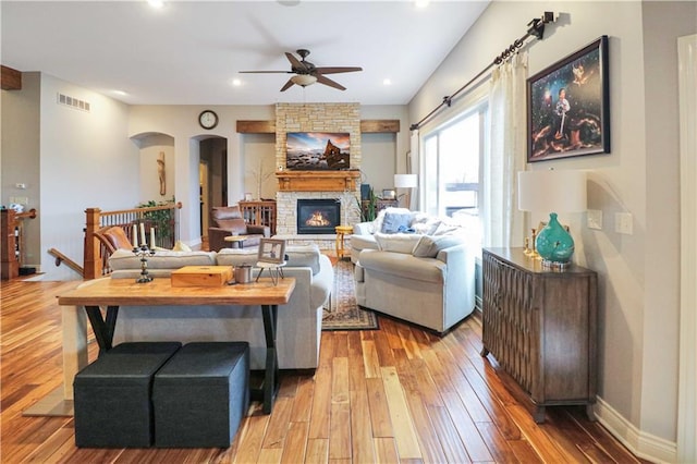 living room featuring light hardwood / wood-style floors, a stone fireplace, and ceiling fan