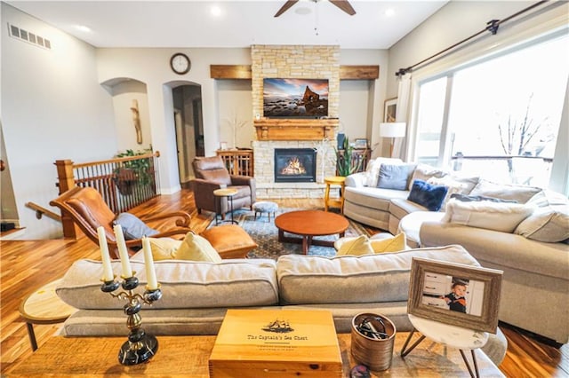 living room featuring wood-type flooring, a stone fireplace, and ceiling fan