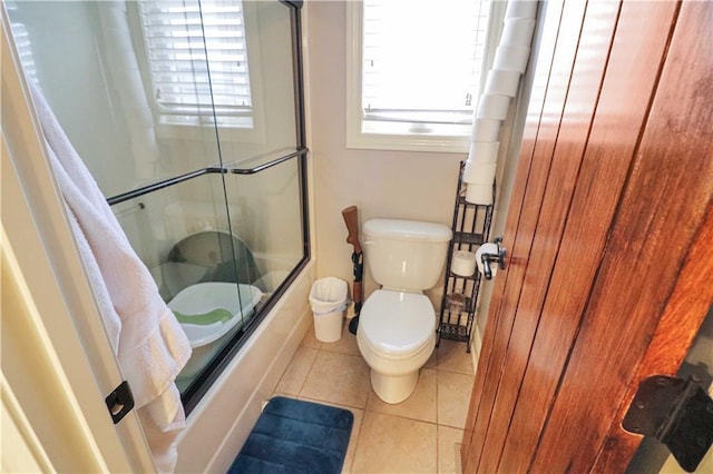 bathroom with toilet, tile patterned floors, and bath / shower combo with glass door