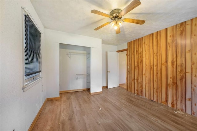 unfurnished bedroom with a closet, ceiling fan, wooden walls, and light wood-type flooring