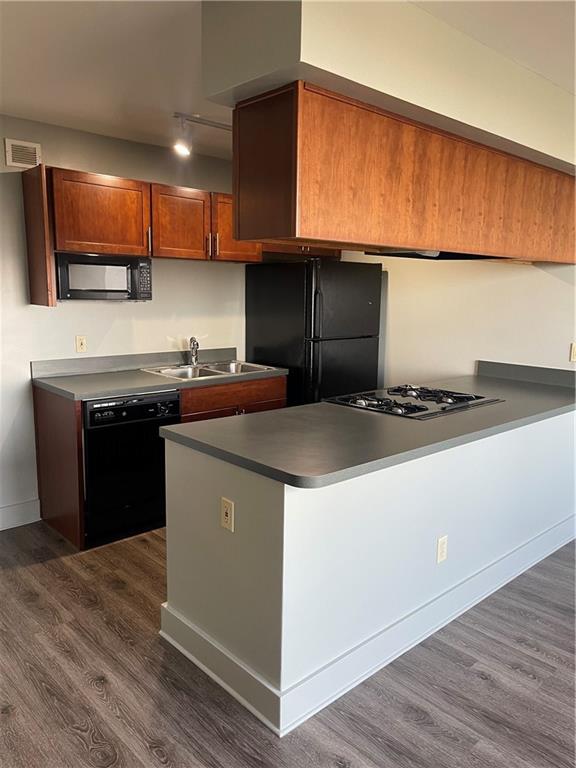 kitchen with kitchen peninsula, dark hardwood / wood-style flooring, sink, and black appliances