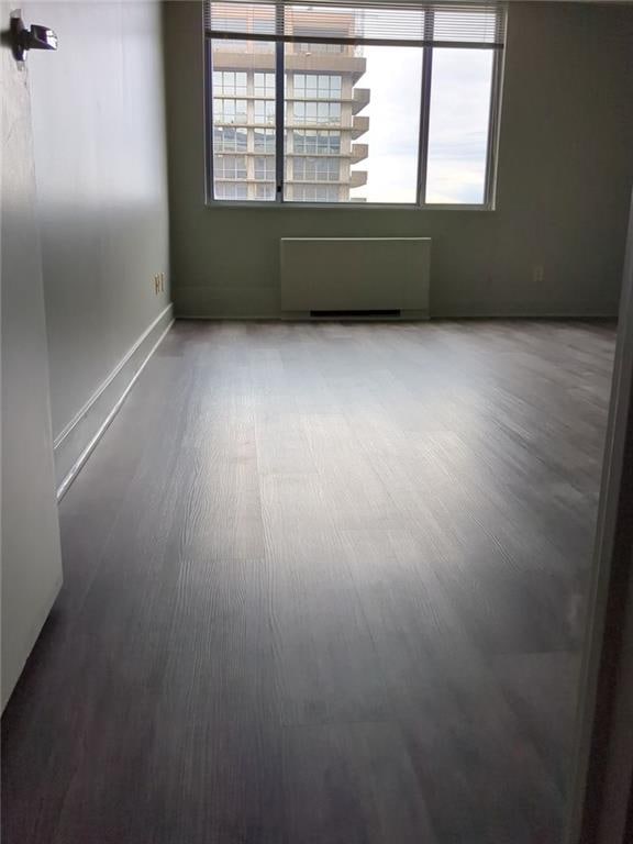 empty room with radiator heating unit, a healthy amount of sunlight, and hardwood / wood-style floors