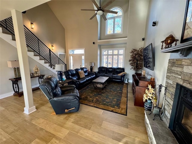 living room with a high ceiling, light wood-type flooring, a stone fireplace, and ceiling fan