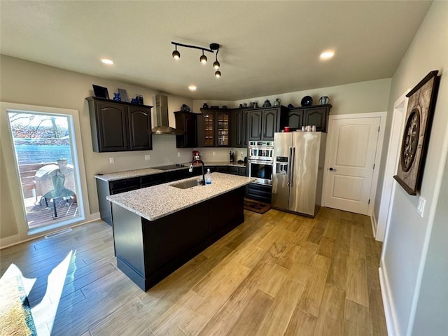 kitchen with dark brown cabinetry, an island with sink, stainless steel appliances, and light hardwood / wood-style floors