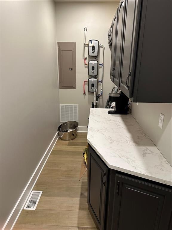 laundry area with electric panel and light hardwood / wood-style flooring