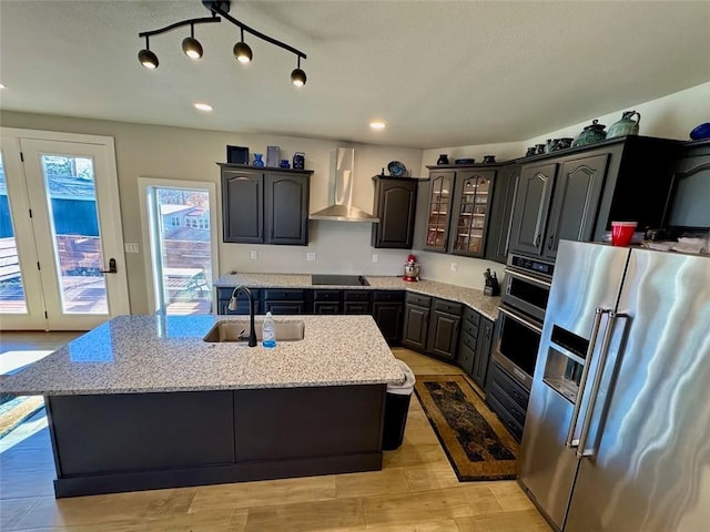 kitchen featuring wall chimney range hood, high quality fridge, sink, and a center island with sink