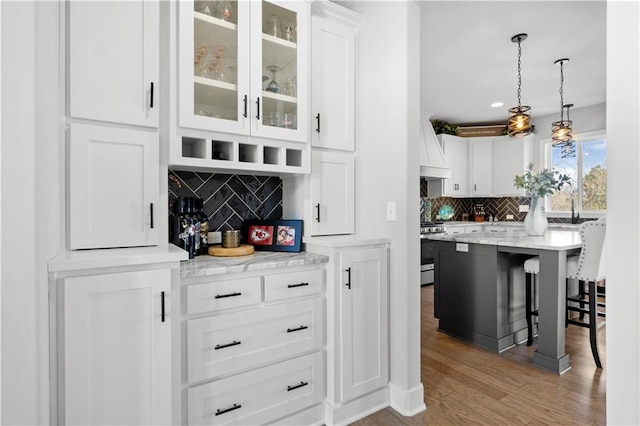 bar with white cabinetry, pendant lighting, light hardwood / wood-style floors, decorative backsplash, and stainless steel stove