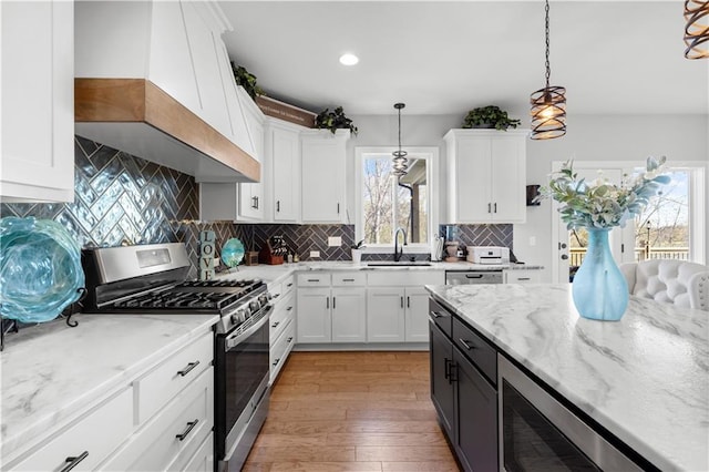 kitchen with pendant lighting, white cabinetry, custom range hood, and stainless steel gas range