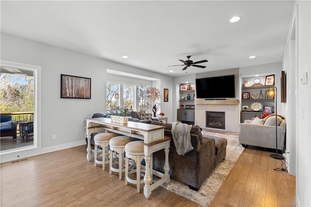 living room with built in shelves, ceiling fan, and light hardwood / wood-style flooring