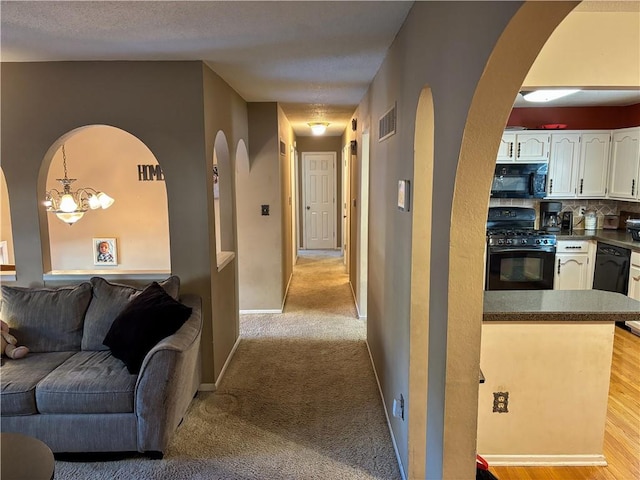 corridor featuring a notable chandelier, light colored carpet, and a textured ceiling