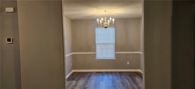 spare room with dark wood-type flooring, a textured ceiling, and an inviting chandelier