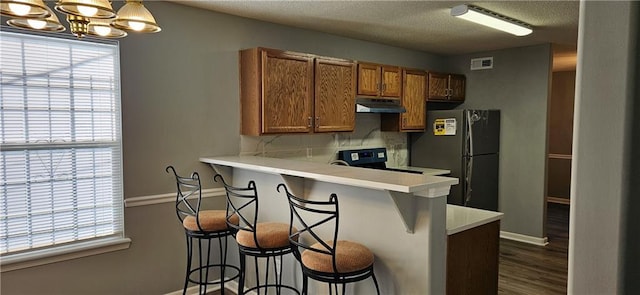 kitchen with kitchen peninsula, stove, stainless steel fridge, pendant lighting, and a breakfast bar area