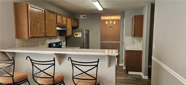 kitchen featuring kitchen peninsula, tasteful backsplash, a breakfast bar, a chandelier, and stainless steel refrigerator