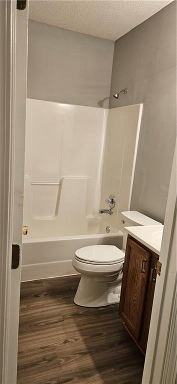 full bathroom featuring a textured ceiling, vanity, shower / bathing tub combination, hardwood / wood-style floors, and toilet