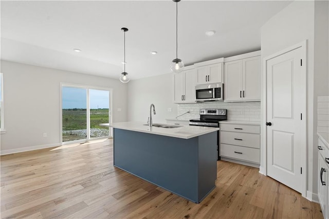 kitchen featuring pendant lighting, appliances with stainless steel finishes, white cabinets, an island with sink, and sink