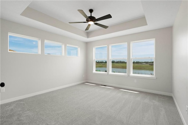 carpeted empty room featuring ceiling fan, a raised ceiling, and a water view