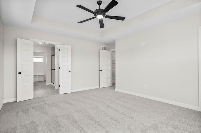 unfurnished bedroom featuring light carpet, connected bathroom, a tray ceiling, and ceiling fan