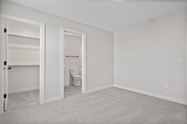 unfurnished bedroom featuring light carpet, a spacious closet, ensuite bath, and a closet