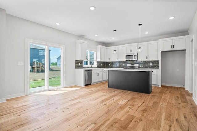 kitchen featuring white cabinets, appliances with stainless steel finishes, a center island, and decorative light fixtures