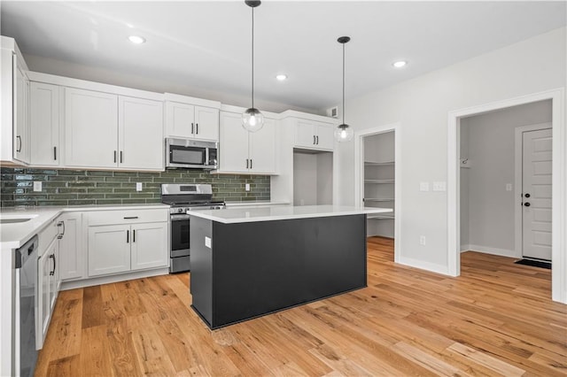 kitchen featuring a center island, appliances with stainless steel finishes, pendant lighting, white cabinets, and light wood-type flooring