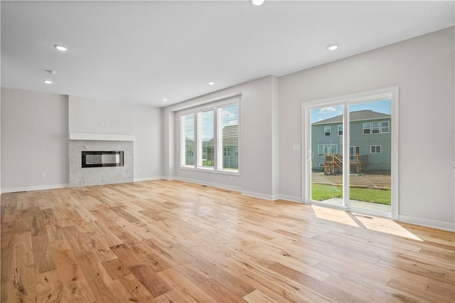 1933 SW Merryman Dr, Lees Summit, MO 64082 - unfurnished living room featuring light wood-style flooring, plenty of natural light, recessed lighting, a glass covered fireplace, and baseboards