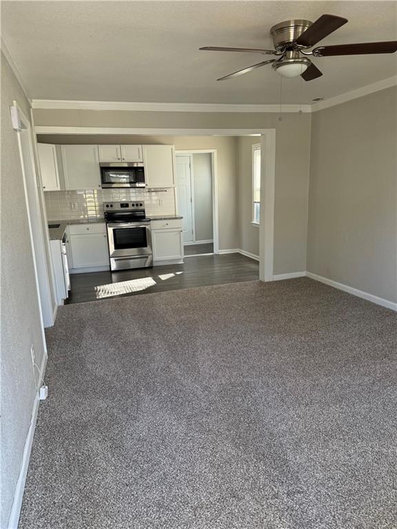 unfurnished living room with ceiling fan, dark carpet, and ornamental molding