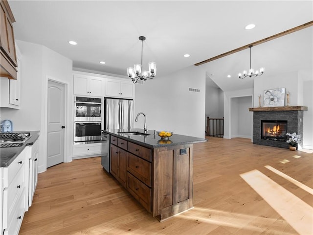 kitchen with white cabinets, a center island with sink, sink, light hardwood / wood-style flooring, and appliances with stainless steel finishes