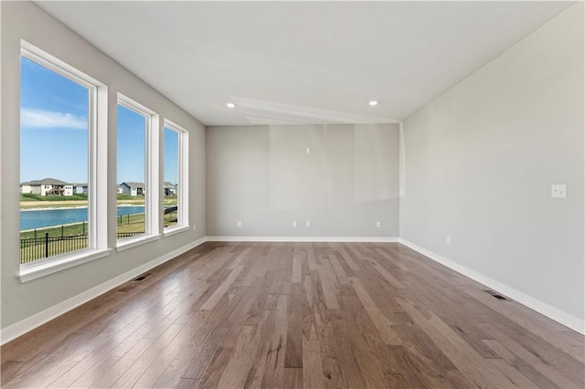 unfurnished room featuring visible vents, a water view, wood finished floors, and plenty of natural light