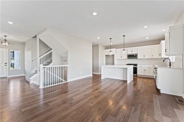 kitchen with hanging light fixtures, stainless steel appliances, a kitchen island, white cabinets, and dark wood-type flooring