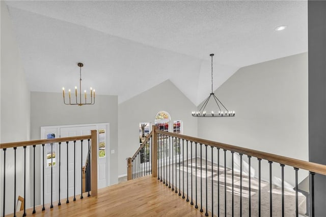 corridor with hardwood / wood-style floors, lofted ceiling, and a notable chandelier