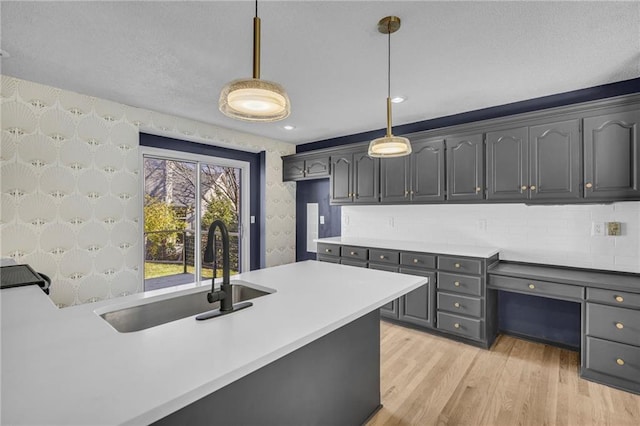 kitchen with sink, pendant lighting, gray cabinets, decorative backsplash, and light wood-type flooring