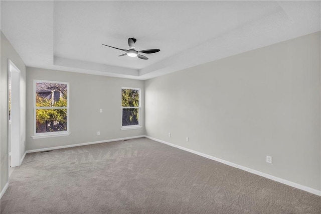 carpeted spare room featuring a raised ceiling and ceiling fan